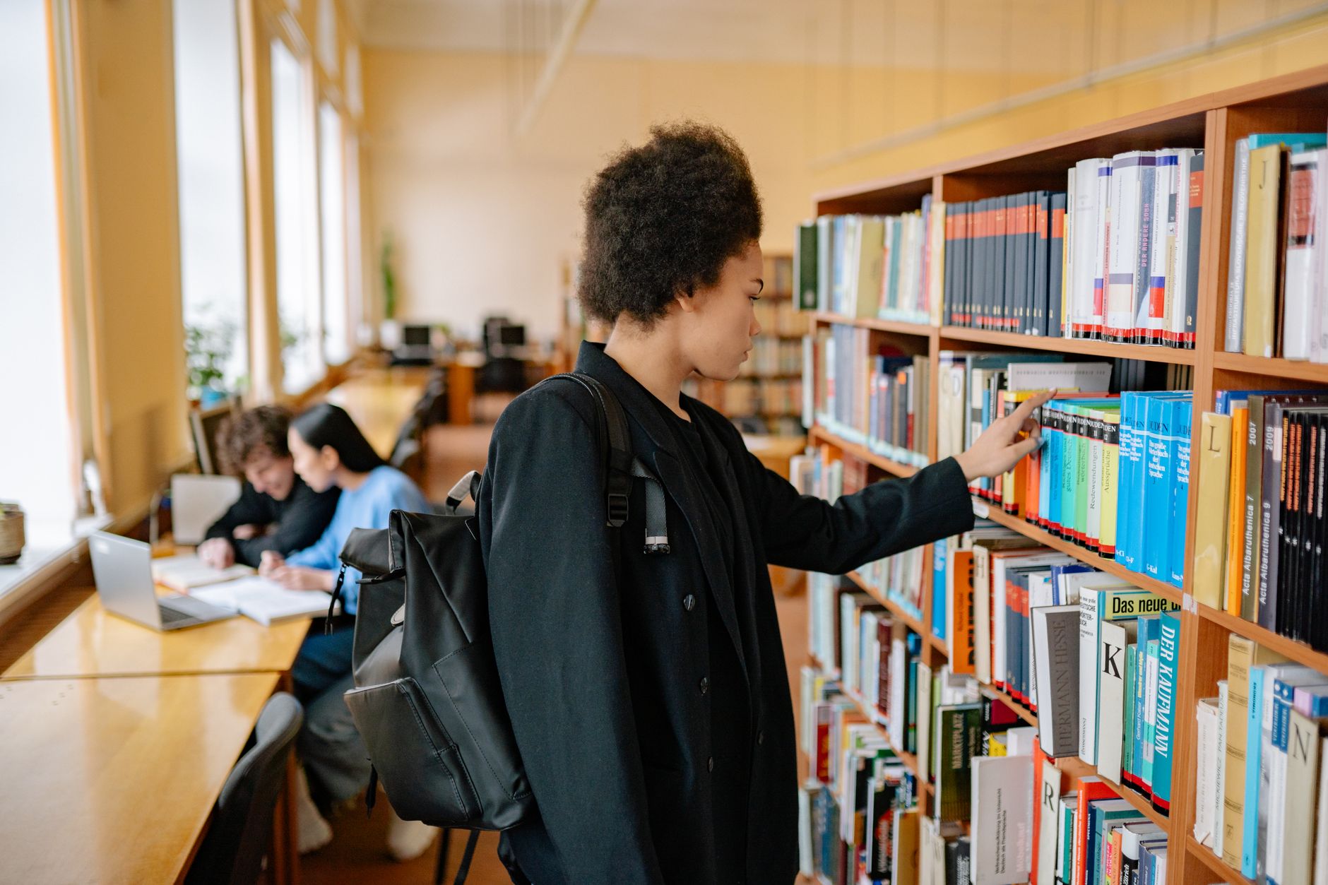 Une étudiante travaille à une table de bibliothèque universitaire, documents et ordinateur portable devant elle.